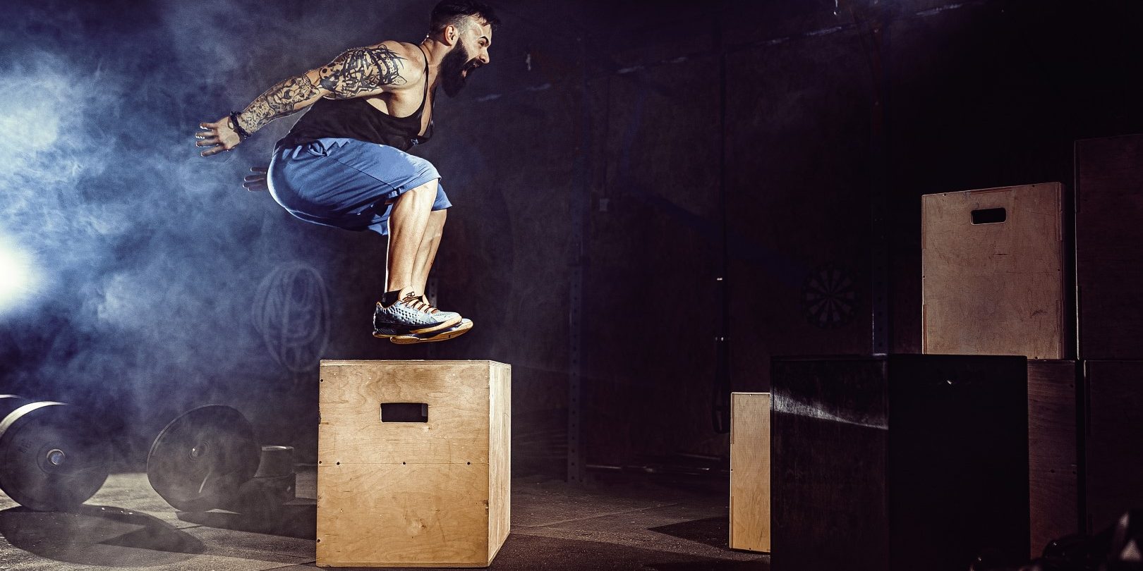 Athlete gave exercise. Jumping on the box. Phase touchdown. Gym shots in the dark tone. Smoke.