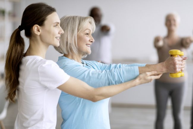 Side view of fitness coach helping senior woman while exercising